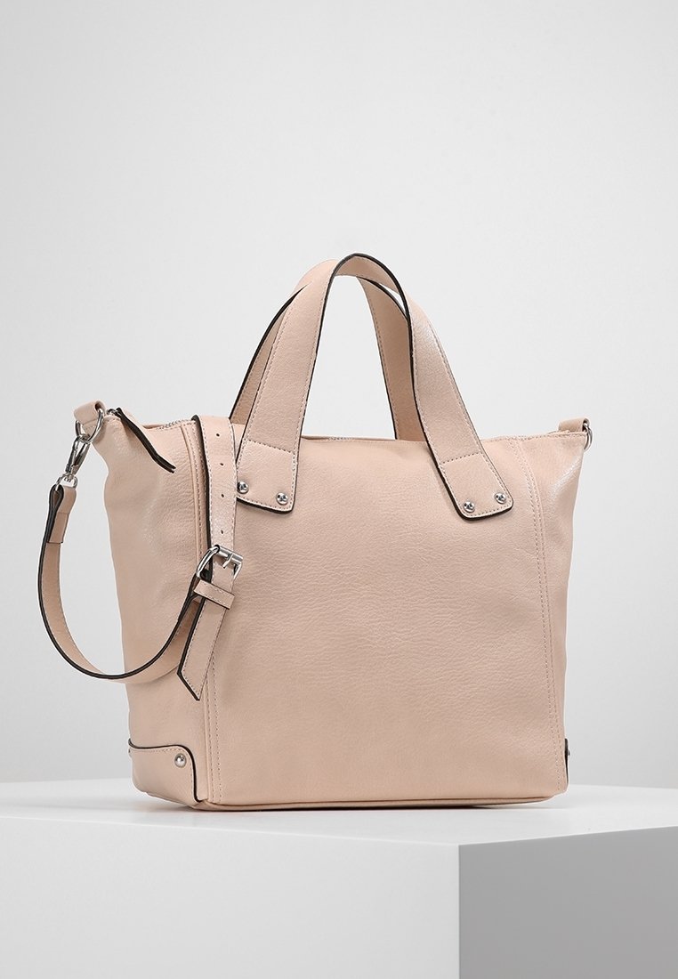 Sac fourre-tout en cuir beige avec double anses, bandoulière amovible, boucles métalliques et coutures minimales sur une surface d'exposition blanche.