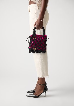 Personne portant un jean court crème et des talons hauts noirs, tenant un sac rose à l'intérieur d'un sac en filet noir avec des détails dorés.
