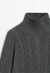 Pull gris foncé à torsades avec un col roulé côtelé haut montrant une texture de tricot détaillée.