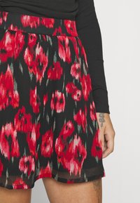 Jupe fleurie noire, avec un motif floral rouge et rose, design plissé et une ceinture à la taille. Tissu léger avec une texture douce.