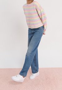 Pull à rayures pastel avec une texture côtelée, associé à un jean bleu à jambes droites et des baskets blanches. Tenue décontractée présentée sur une surface rose.