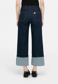 Jeans de pierna ancha con un cuerpo de mezclilla oscura y puños de mezclilla clara en contraste; incluye bolsillos traseros y detalles de costura visibles.