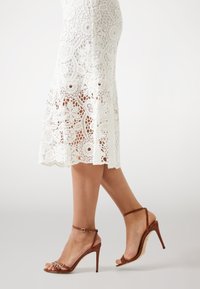 White lace skirt with floral patterns and scalloped hem paired with brown strappy high-heeled sandals, showcasing a smooth finish.