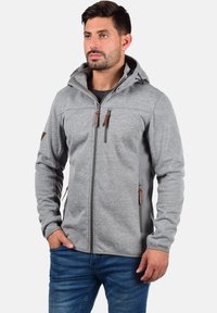 Veste en polaire grise avec capuche, dotée de panneaux latéraux gris foncé, de tirettes en cuir marron et de deux poches poitrine zippées.