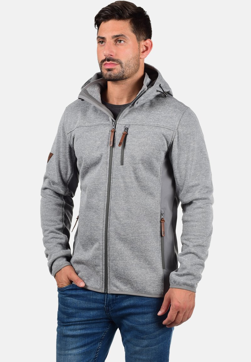 Veste en polaire grise avec capuche, dotée de panneaux latéraux gris foncé, de tirettes en cuir marron et de deux poches poitrine zippées.