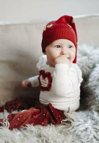 Cappello a maglia rosso con punta, camicia bianca a maniche lunghe con dettaglio a cuore testurizzato e pantaloni morbidi rossi con motivi a cuore dorati.