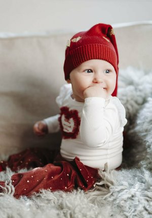Cappello a maglia rosso con punta, camicia bianca a maniche lunghe con dettaglio a cuore testurizzato e pantaloni morbidi rossi con motivi a cuore dorati.