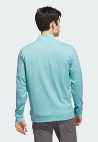 Světlomodrá polokošile s dlouhým rukávem a límečkem. Hladká textura a přiléhavý střih, s elastickými manžetami a rovnou lemem.