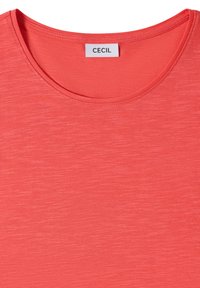 T-shirt corail à col rond avec une texture chinée subtile et une étiquette blanche portant la mention "CECIL" cousue à l'intérieur du col.