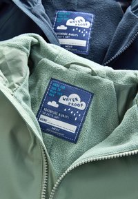 Kaksi vedenpitävää takkia fleece-vuorella ja sinisillä merkeillä, joissa lukee "Made for you to keep you dry" ja "Adventure awaits, so let's go!"