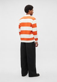 Pulôver às riscas em laranja e branco com um corte descontraído, combinado com calças pretas de perna larga. Gola e punhos canelados, textura macia de algodão.