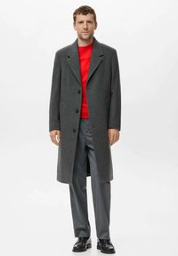 Siv wool mantelj s širokimi reverji in tremi gumbi, oblečen čez svetlo rdečo pulover. V kombinaciji s sivimi hlačami in črnimi čevlji.