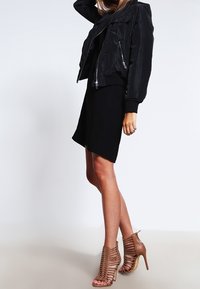 Černá bomber bunda se zipy, nošená přes černé šaty. Stylizováno s tanovými, vysokými sandály na podpatku s řemínky. Jednoduchá, moderní silueta.