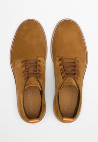 Chaussures à lacets en daim marron avec une texture lisse, un bout rond et une semelle cousue de couleur claire contrastante. Accent en cuir au talon.
