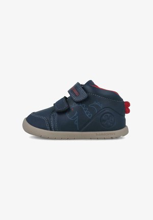 Zapatos de cuero azul para niños con detalles rojos, correas de velcro, estampado de dinosaurios y una suela de goma beige con un detalle de logo en el costado.