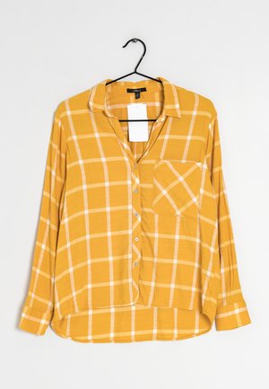 Keltainen ruudullinen pitkähiha shirtti, jossa on kaulus, nappikiinnitys, yksi rintatasku ja valkoinen ruutukuvio. Pehmeä kangas ja rento mitoitus.