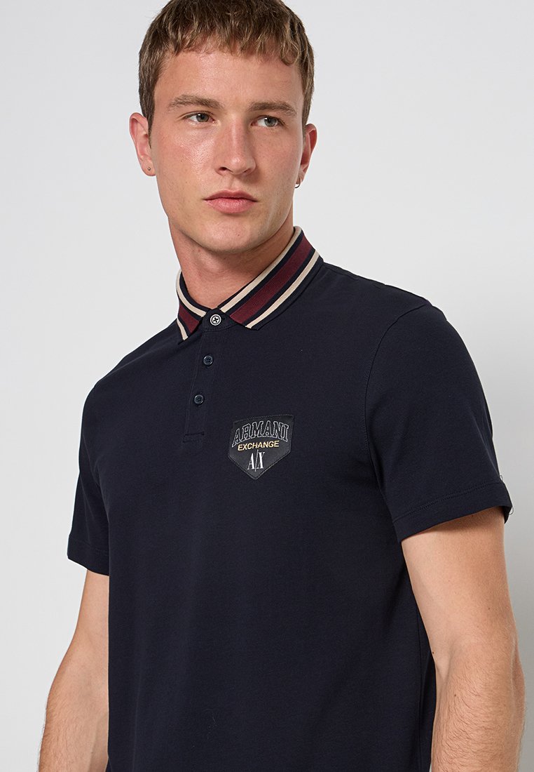 Marineblauwe polo gemaakt van katoen, met een gestreepte kraag in bordeaux en crème, een placket met drie knopen en een geborduurd logo-patch.