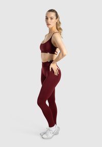 Un reggiseno sportivo bordeaux e leggings a vita alta realizzati in tessuto elasticizzato, con una texture liscia e un design minimalista. Scarpe da ginnastica bianche.