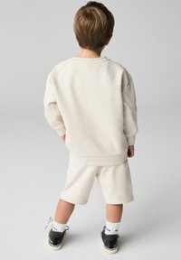 Kremefarvet oversized sweatshirt parret med matchende shorts, begge i et blødt stof, designet med en afslappet pasform. Sorte sneakers båret med hvide sokker.