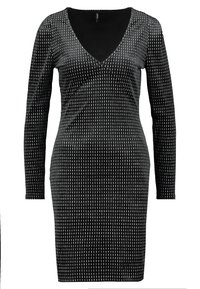 Svart långärmad klänning med djup V-halsringning, prydd med ett prickigt mönster i vitt. Tillverkad av ett slätt, elastiskt material.