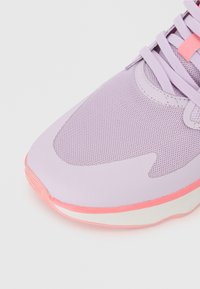 Αθλητικό παπούτσι σε ανοιχτό μωβ χρώμα με πλέγμα επάνω, επισημασμένο από ροζ καουτσούκ σόλα και κορδόνια, διαθέτοντας κομψό αεροδυναμικό σχέδιο.