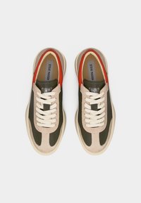 Paire de baskets basses avec panneaux beige, vert et rouge, lacets blancs, et logo Steve Madden sur les semelles intérieures, vues de dessus.