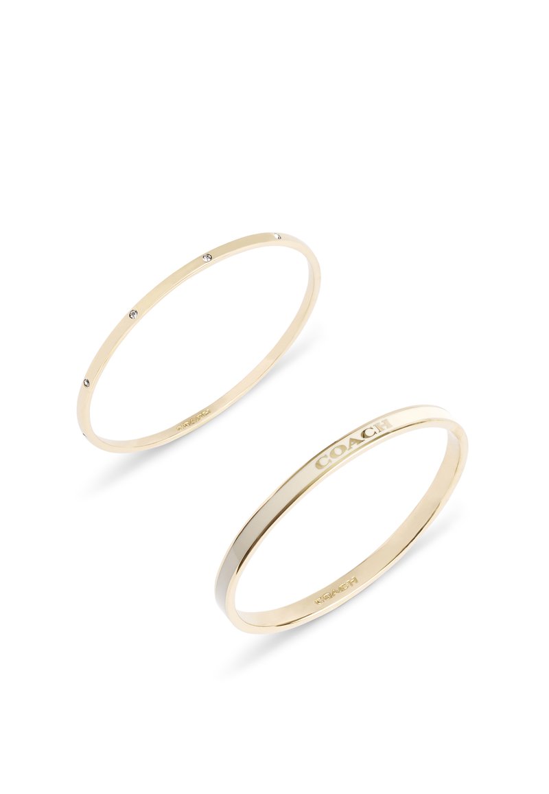 Brazaletes de brazalete chapados en oro; uno presenta tres pequeñas piedras transparentes, el otro tiene un logo grabado. Acabado liso y pulido, forma circular.