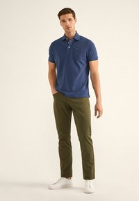 Polo azul marino con cuello y bolsillo en el pecho, combinado con pantalones ajustados verde oliva y zapatillas blancas. Textura de tela suave.