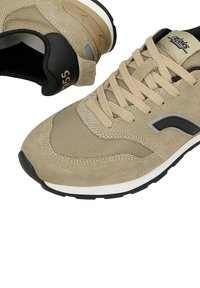 Beige Wildledersneaker mit schwarzen Akzenten, Netzpaneelen und einer strukturierten Sohle. Mit runden Schnürsenkeln und seitlicher Logo-Detailierung.