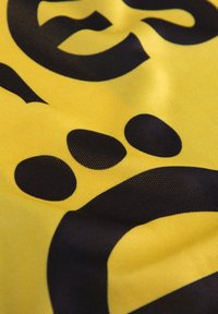 Geel fabric met gedurfde zwarte grafische elementen, waaronder letters en cirkels. Het materiaal lijkt glad met een lichte glans.