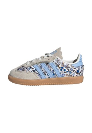 Baskets basses avec un bout et un talon en daim beige, rayures bleu clair, tissu floral bleu et blanc, et une semelle en caoutchouc gomme.