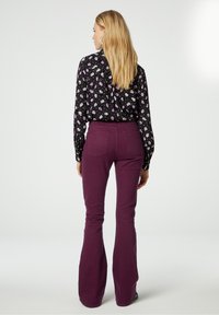 Vloeiende zwarte blouse met een wit en paars bloemmotief, gecombineerd met hoog.mapreduce, uitlopende, pruimkleurige broek. Glad stoftextuur.