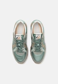 Paire de baskets vertes et beige à lacets avec des détails en daim et en cuir, vues de dessus sur un fond clair uni.