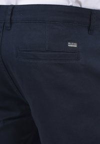 Pantalon en coton bleu marine comprenant une poche au dos et une étiquette argentée "BLEND". Texture lisse avec un design épuré.
