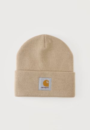 Bonnet beige en tricot avec revers plié et un écusson carré affichant le logo Carhartt en jaune et blanc au centre avant.
