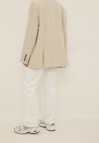 Beige blazer met gestructureerde schouders, witte rechte jeans en grijze sneakers met zwarte accenten en mesh-details.