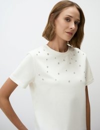 Weißes Kurzarm-T-Shirt mit glatter Textur, das auf der Vorderseite verstreute Strasssteinakzente für subtile Details aufweist.