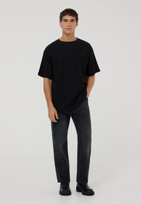 T-shirt nera oversized con maniche corte, abbinata a jeans di denim scuro e stivali neri con suola spessa. Design semplice e minimalista.