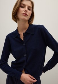 Marineblauwe cardigan van textuur gebreide stof, met een kraag, knopen aan de voorkant en een cropped ontwerp met lange mouwen.