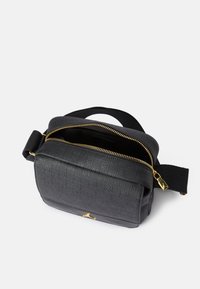 Svart skulderveske i preget materiale med gullglidelås. Har en flat strop og to rom for oppbevaring. Teksturert overflate og logodetalj.