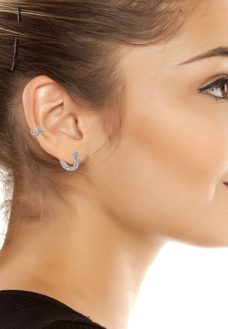 Boucles d'oreilles argentées en forme de croissant, l'une d'elles ornée de petites pierres précieuses transparentes. Design courbé, texture lisse, portées à la fois sur la partie supérieure et inférieure de l'oreille.