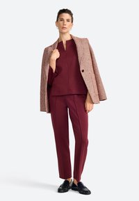 Costume deux pièces bordeaux avec un blazer à carreaux texturé et un pantalon droit ; associé à des mocassins noirs. Tissu lisse, coupe ajustée.