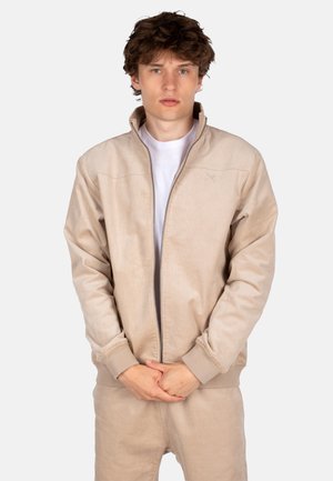 Beige Bomberjacke mit Reißverschluss aus weichem Stoff, mit gerippten Bündchen und Kragen. Schlichtes Design mit minimalen Nähten und lockerer Passform.