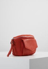 Bolso de cuero rojo con cierre de cremallera y bolsillo frontal. Presenta una superficie texturizada y detalles decorativos en la cremallera. Forma rectangular compacta.
