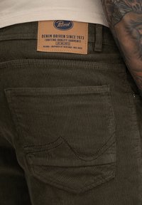 Olijfgroene corduroy broek met een zichtbare achterzak, voorzien van een vierkant label met de tekst "Petrol" en decoratieve stiksels.