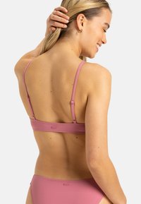 Różowy stanik bikini z regulowanymi cienkimi ramiączkami, gładką fakturą i metką marki z tyłu. Prosty design i dopasowany kształt.