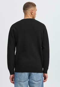 Svart strikket genser med rund hals, lange ermer og ribbestrikkede mansjetter, kombinert med lyseblå denimjeans. Enkel, strukturert design.