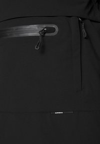 Gros plan d’un tissu noir avec deux poches zippées dotées de joints étanches et une petite étiquette de la marque « Icepeak ».