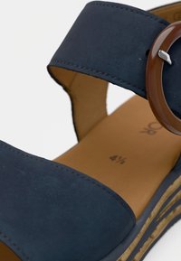 Navy blue suede sandal with a wide strap, round brown accent buckle, and a cork-like platform sole. Smooth inner lining with size detail.