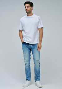 Camiseta de algodón blanca combinada con jeans rasgados de color azul claro y zapatillas blancas. El conjunto presenta un corte relajado y un diseño casual.